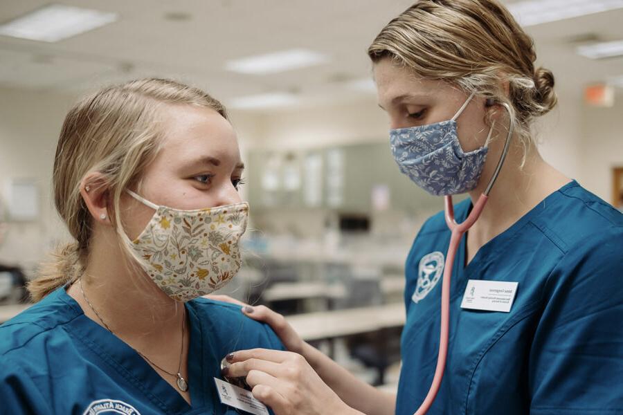 a nursing student listening to the heartbeat of another student through a stethoscope